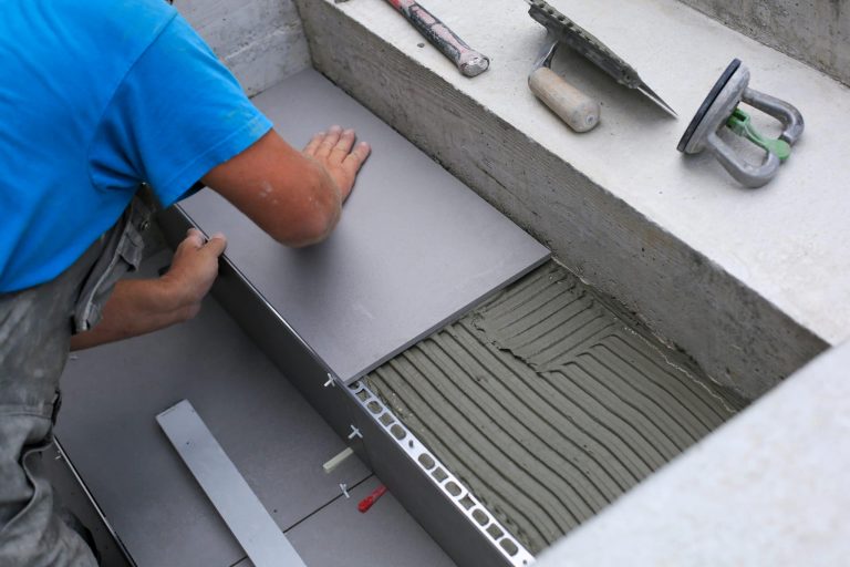 Tiler hands working on a new house entrance by installing aluminium trim
